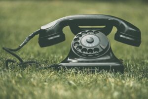 A classic black rotary dial telephone resting on green grass, highlighting vintage style.